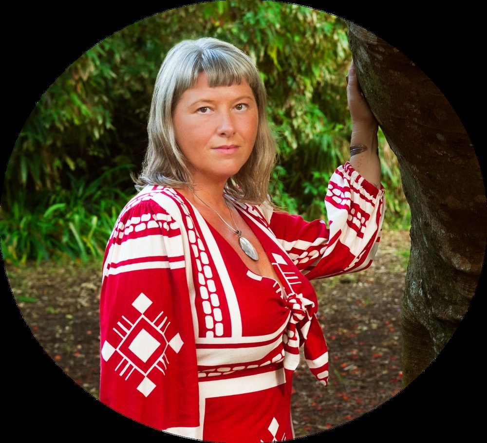 Ananda Leigh in a red dress, resting a hand against a tree